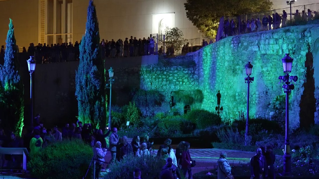 Crowd gathered below the wall lit in green and blue